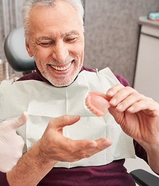 A smiling, older man assessing dentures provided by a dentist