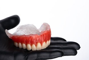 Gloved hand holding a wax denture