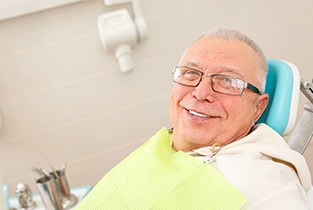 Senior man with glasses sitting in dental chair and smiling