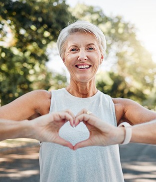 Lady smiles outdoors while making shape of heart with her hands