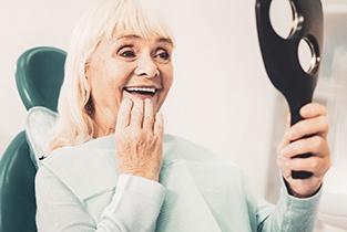 happy mature woman looking in mirror at dentist  
