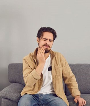 Man sitting on sofa, suffering from a toothache