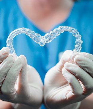 Dentist holding two aligners for Invisalign in Rio Rancho, NM in a heart shape
