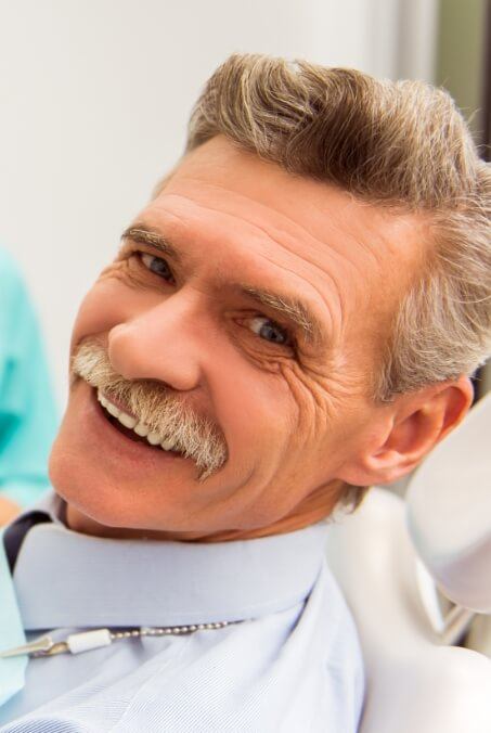 Smiling man in dental chair after replacing missing teeth