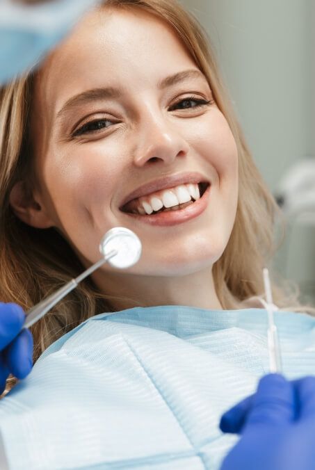 Woman in dental chair smiling after restorative dentistry treatment