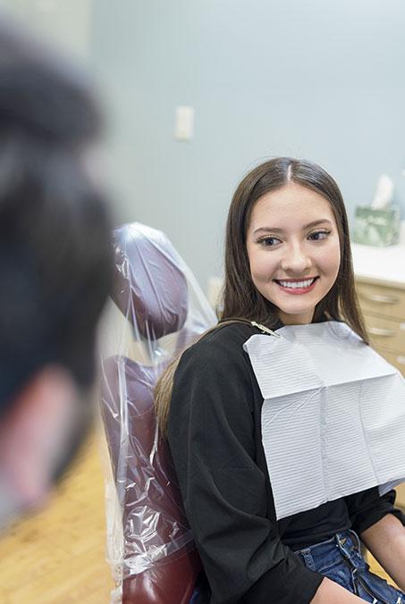 Woman in dental chair smiling after restorative dentistry treatment