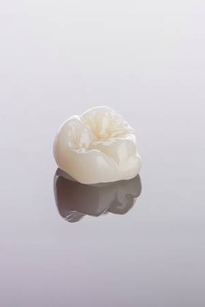 Ceramic dental crown sitting on reflective surface