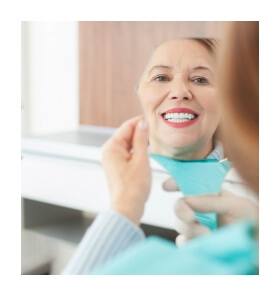 Woman looking at smile in mirror during preventive dentistry visit
