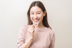 Smiling woman holding Invisalign aligner close to her mouth 