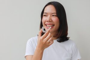 Woman smiling while putting on her clear aligners