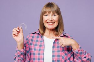 Older woman smiling and holding her Invisalign tray